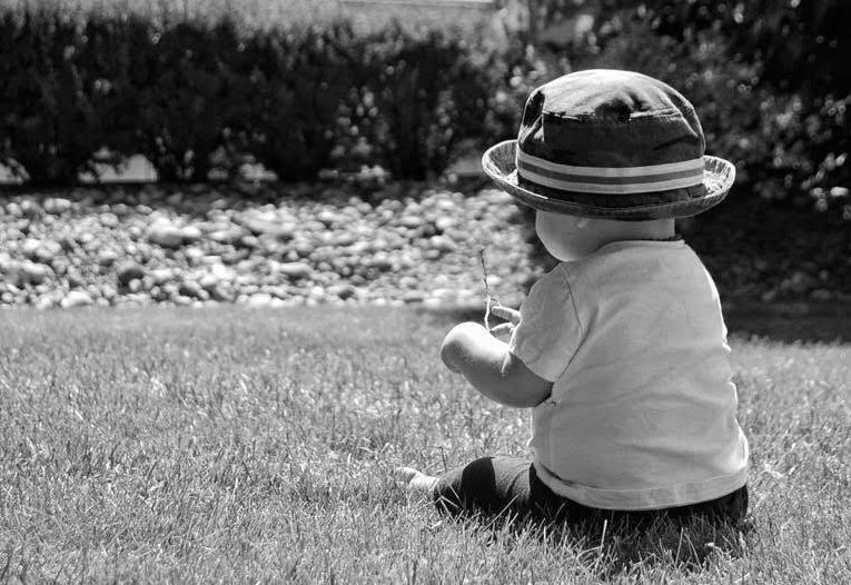 A baby sitting in the grass wearing a hat.