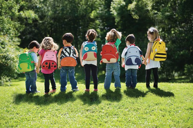 A group of children with backpacks standing in the grass.