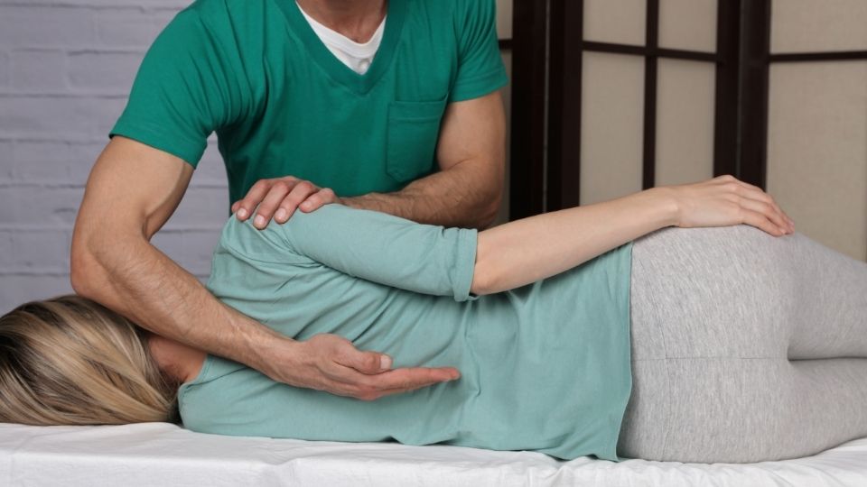 A person is stretching on the bed while another person holds their arm.