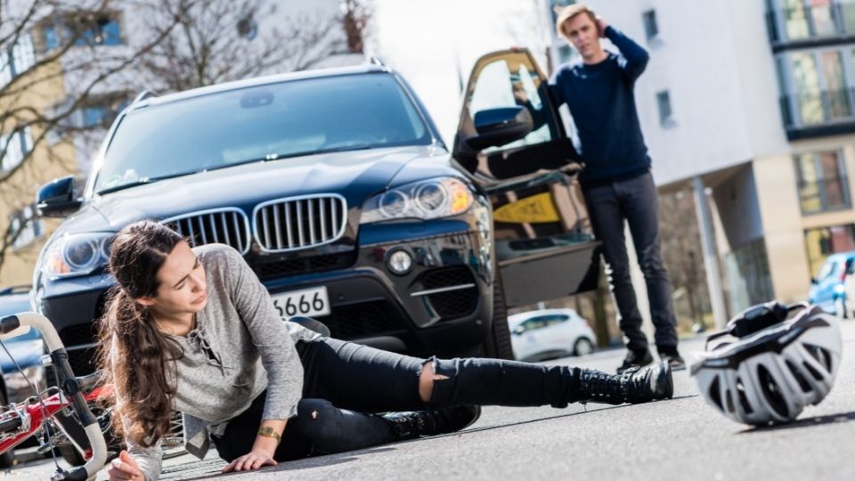 A woman is lying on the ground in front of a car.