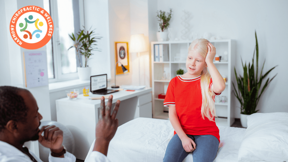 A young girl sitting on the bed with her hand up to her head.