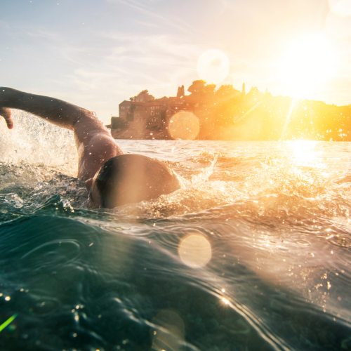 man swimming in the ocean with the sun in the background