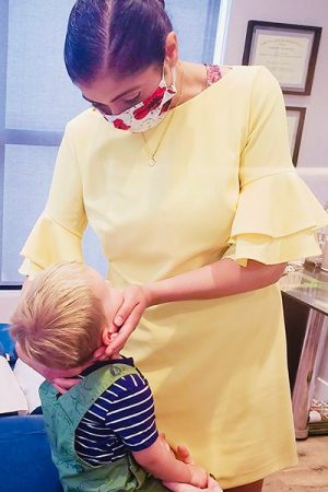 A woman in yellow dress putting on a child 's face.